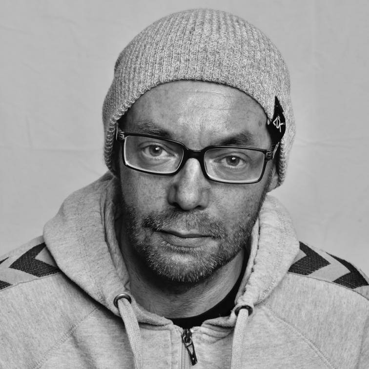 Tom Ole Alvær i grå lue, briller og hettegenser ser rett i kameraet. Svart-hvitt.